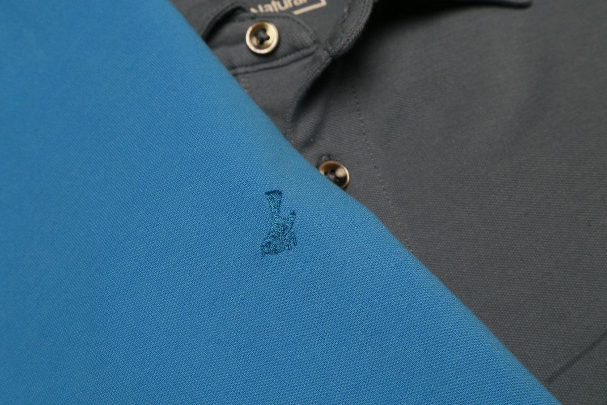 Close-up of teal HyperNatural piqué polo with bird logo beside a charcoal polo collar